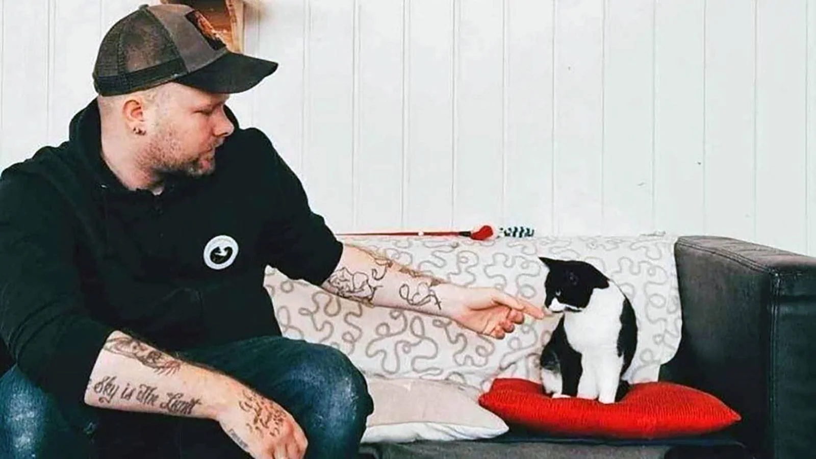 Robin Eide sitter i en sofa sammen med en svart og hvit katt. Han rekker hånden frem til katten.