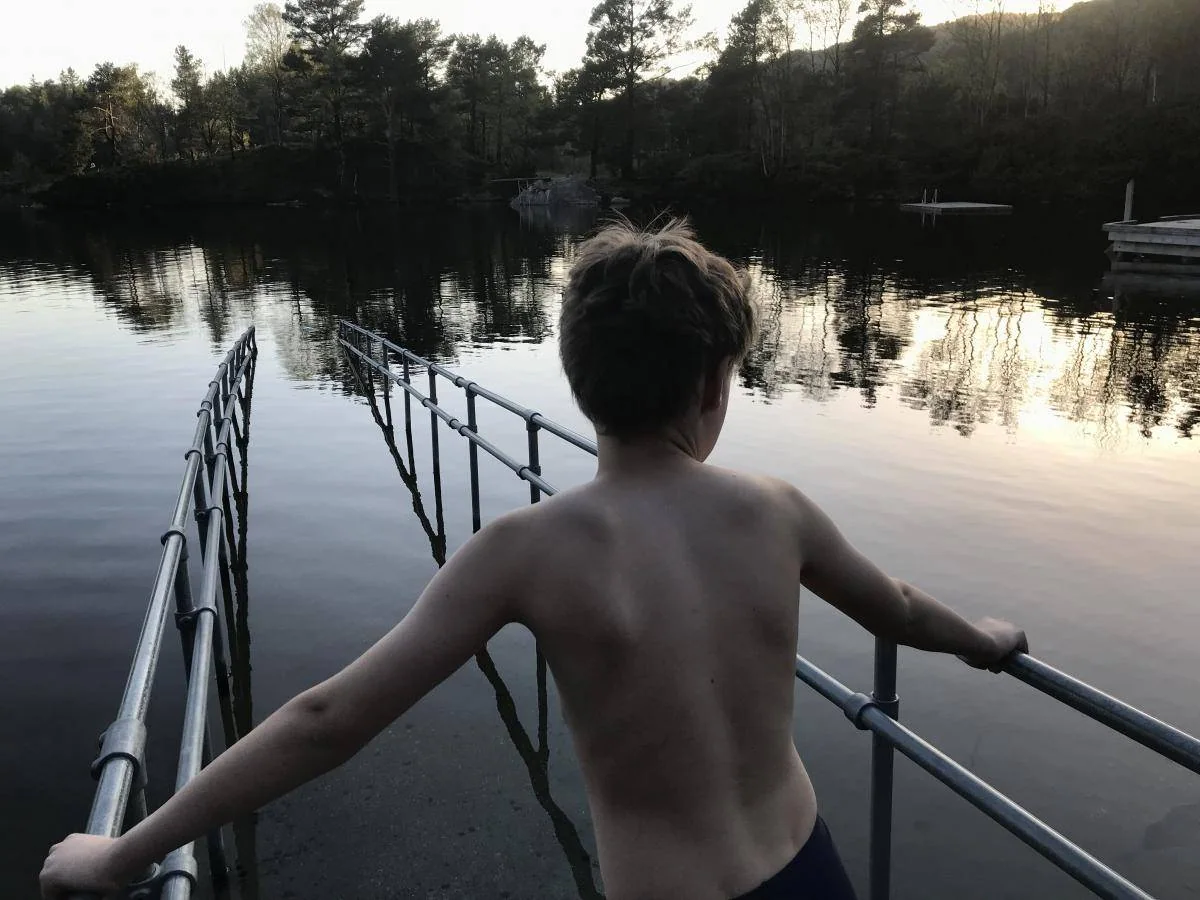 Et barn ser utover en innsjø fra en brygge med rekkverk.