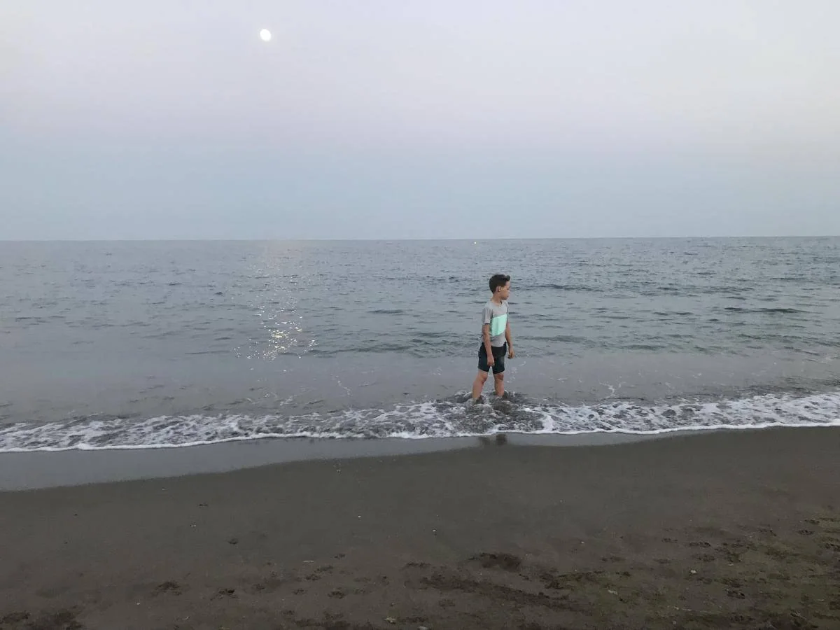 Et barn går langs vannkanten ved havet.