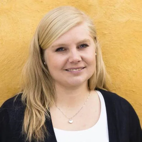 Portrett av en kvinne med lyst hår foran en gul vegg.