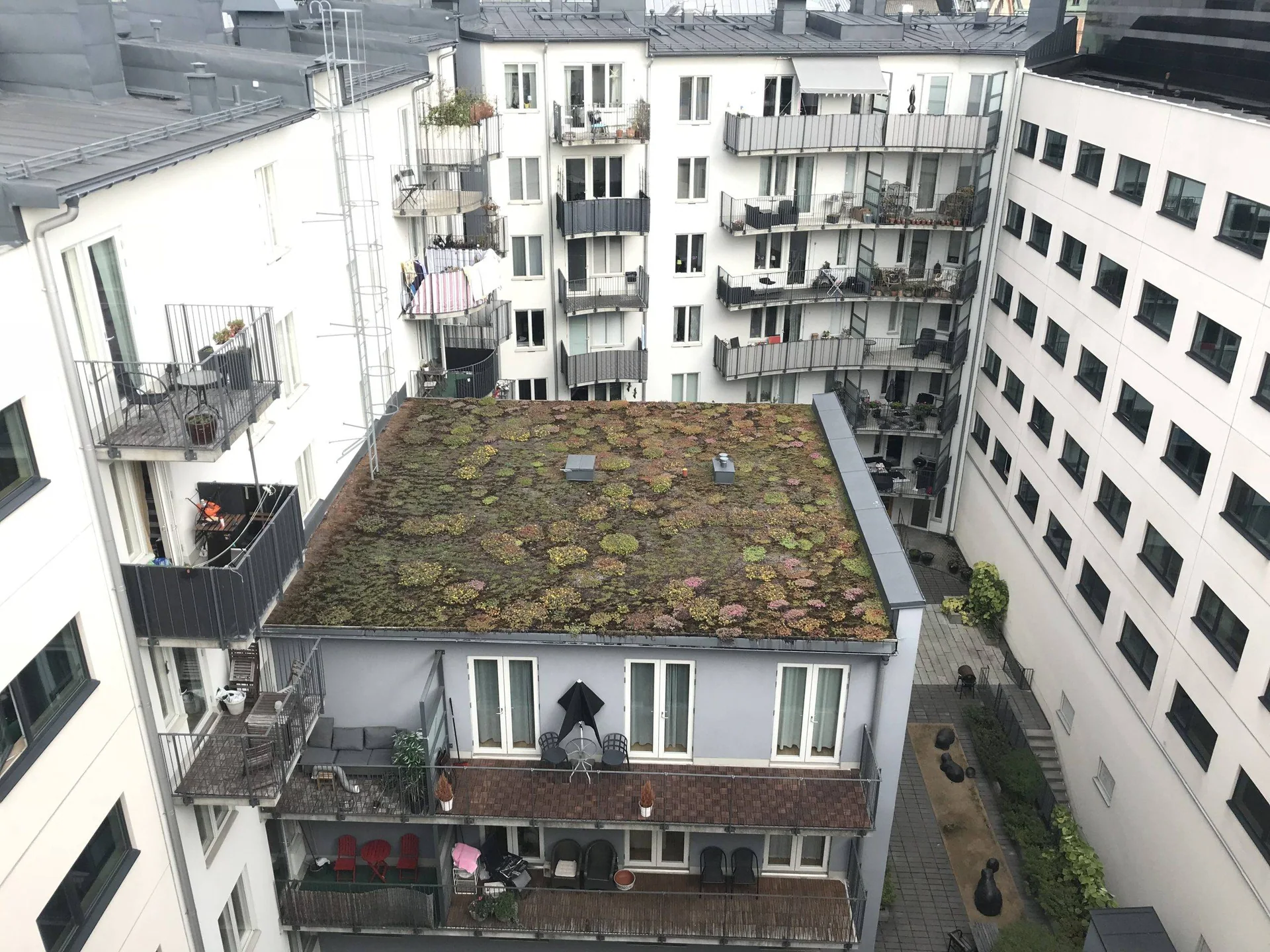 Utsikt over en bakgård med en lav bygning omgitt av boligblokker.