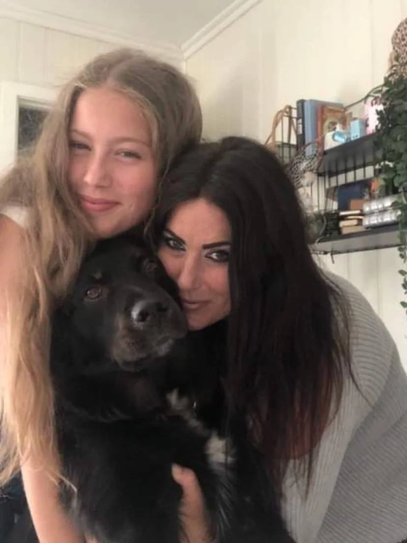 To kvinner holder rundt en svart hund.