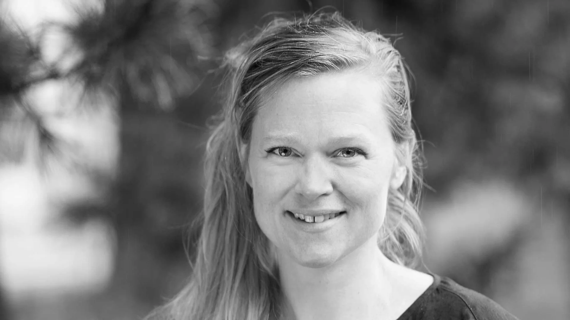 Svart-hvitt-portrett av en smilende kvinne utendørs.