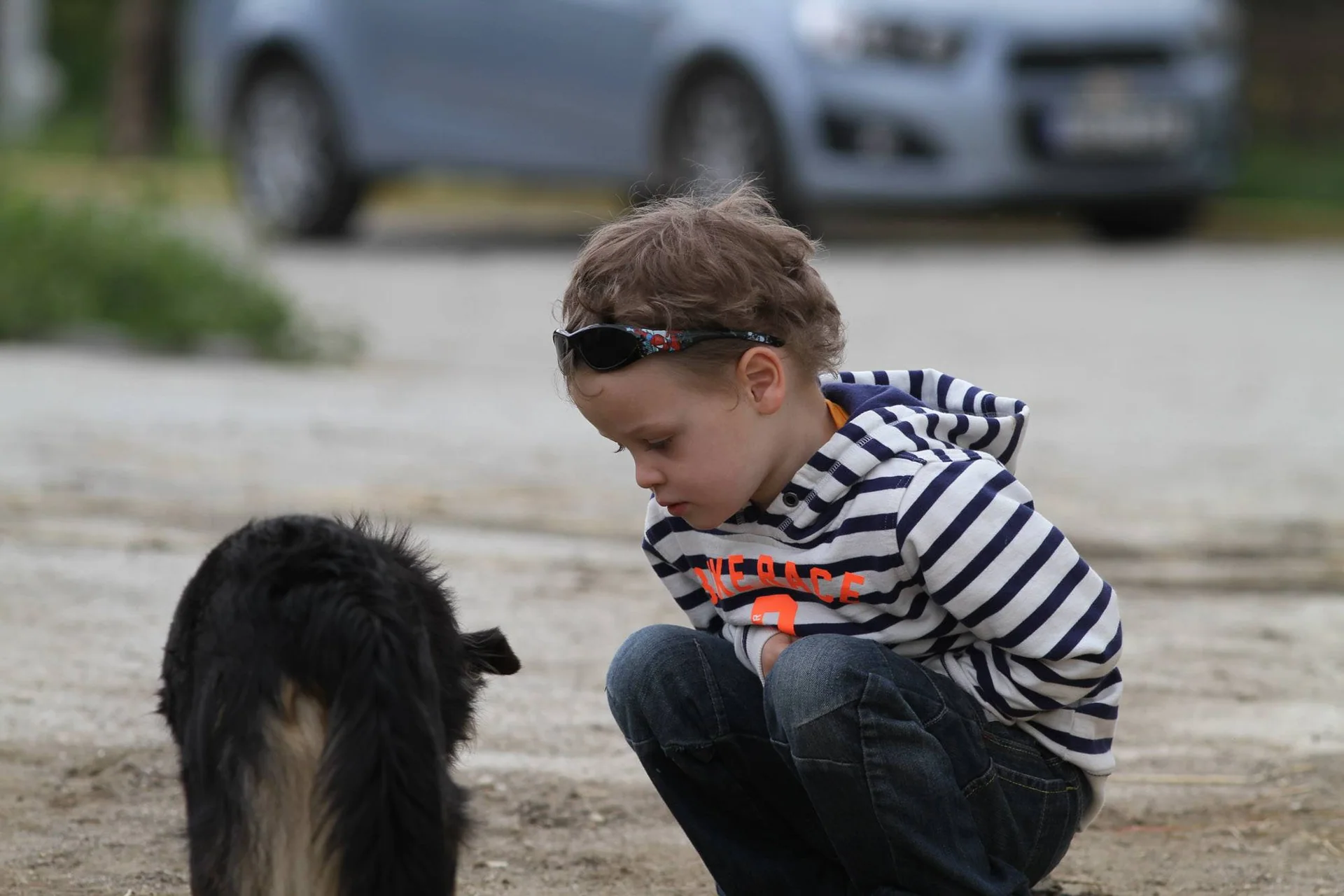 Et barn sitter på huk ved en svart og hvit hund utendørs.