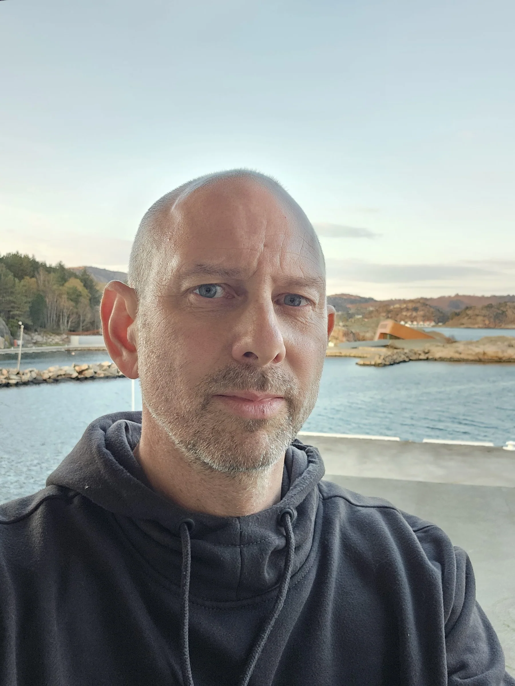 Portrett av en mann i mørk hettegenser med sjøen i bakgrunnen.