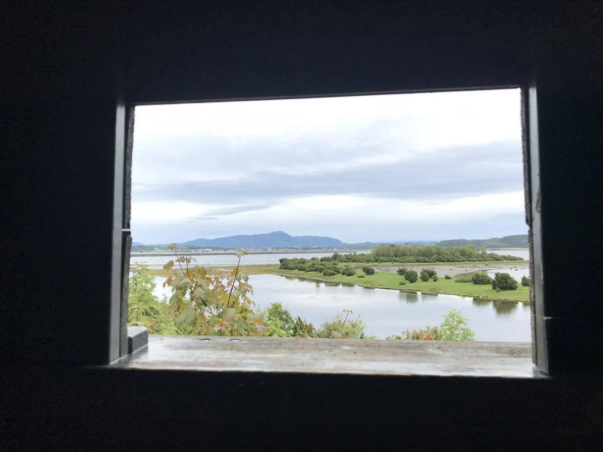 Et vindu rammer inn utsikten over en elv, grønne øyer og fjell.