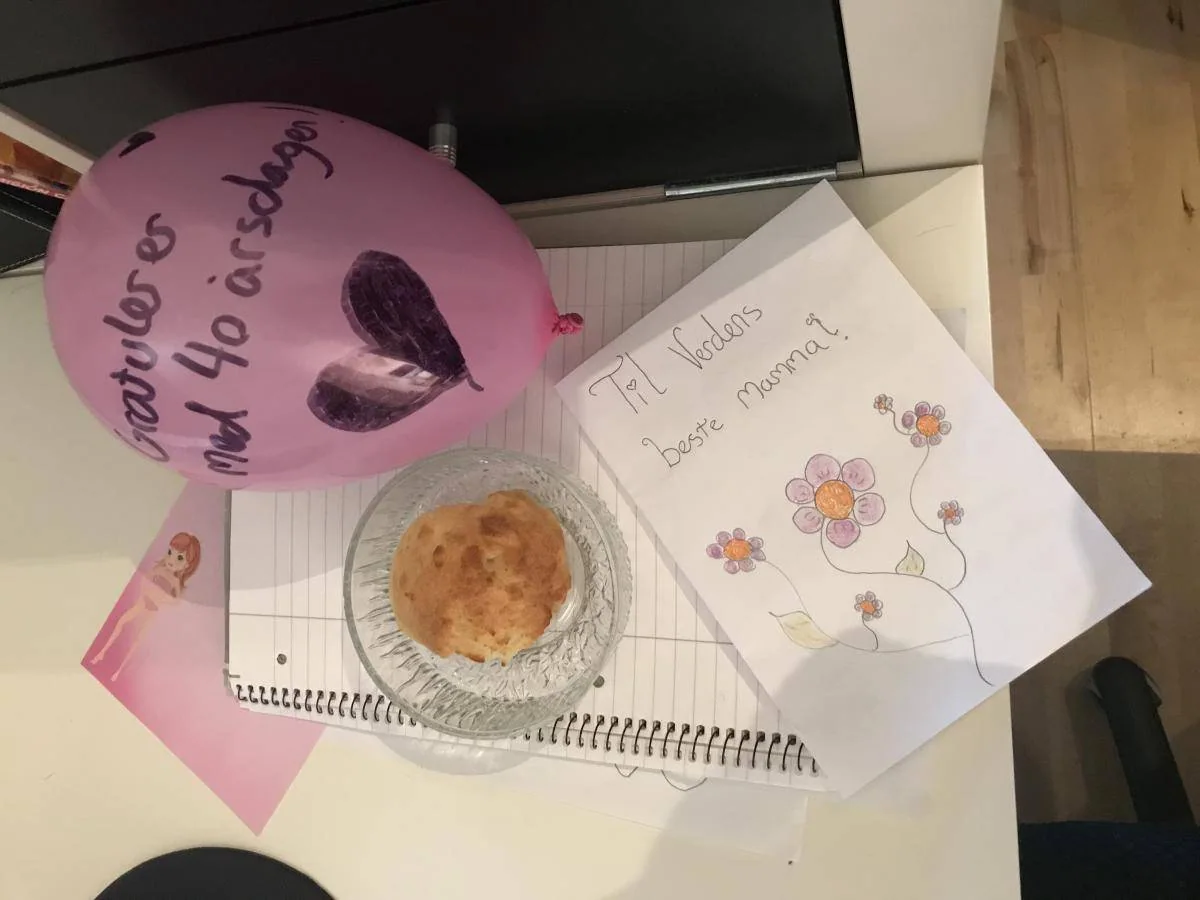 En rosa bursdagsballong, et håndskrevet kort og en muffins ligger på et bord.