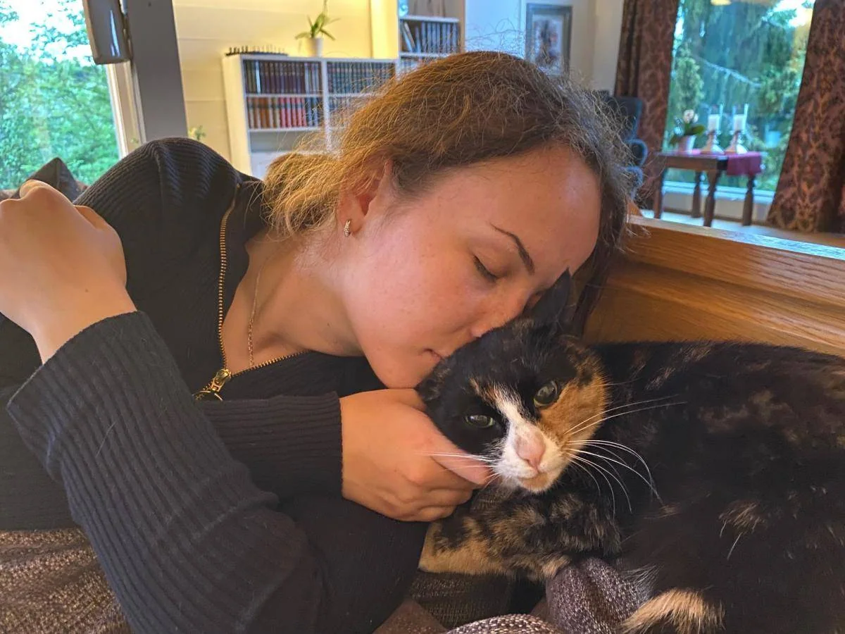 En kvinne kysser en trefarget katt som ligger i armene hennes.