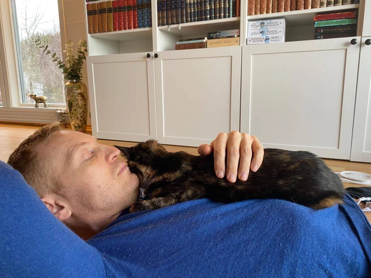 En person ligger på gulvet med lukkede øyne og en katt på brystet.