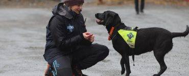 Marie Berntsen sitter på huk foran den svarte labradoren Leo, som er redningshundelev, og skryter av innsatsen.
