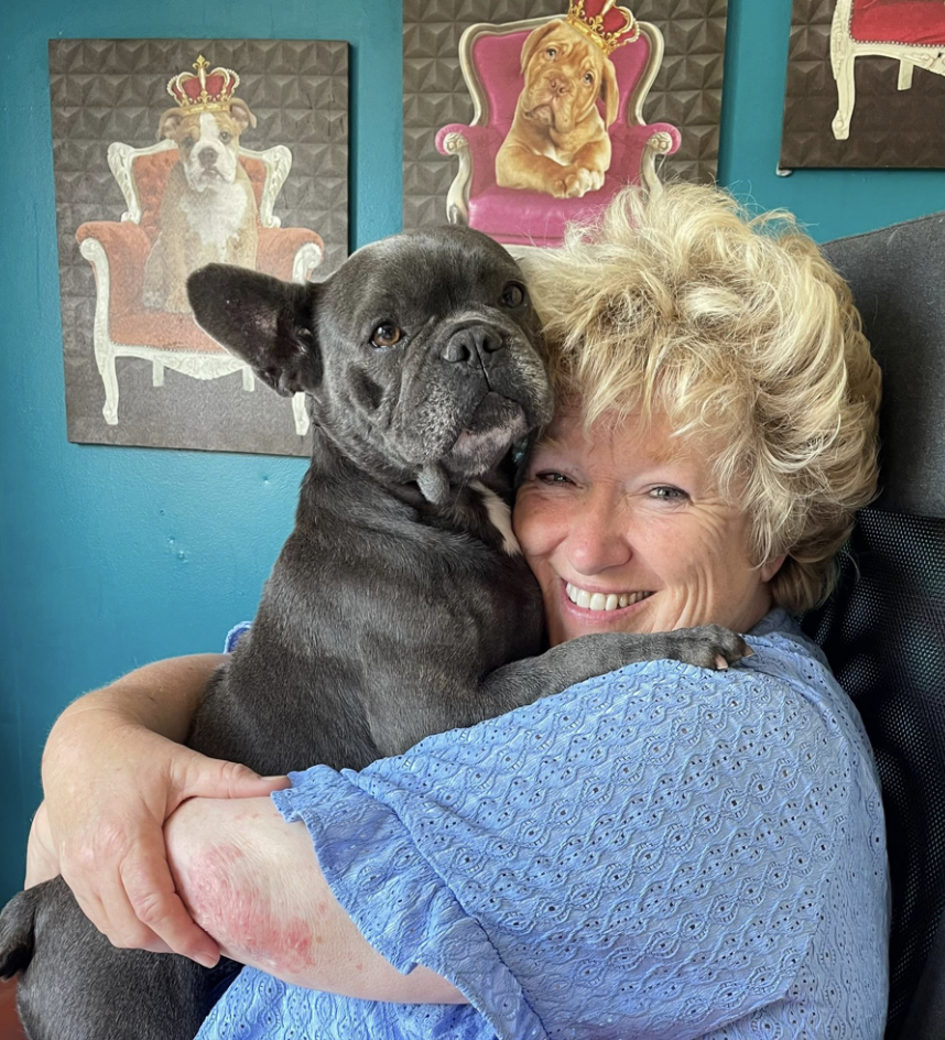 Fabienne Paques smiler og holder rundt en svart, liten hund.
