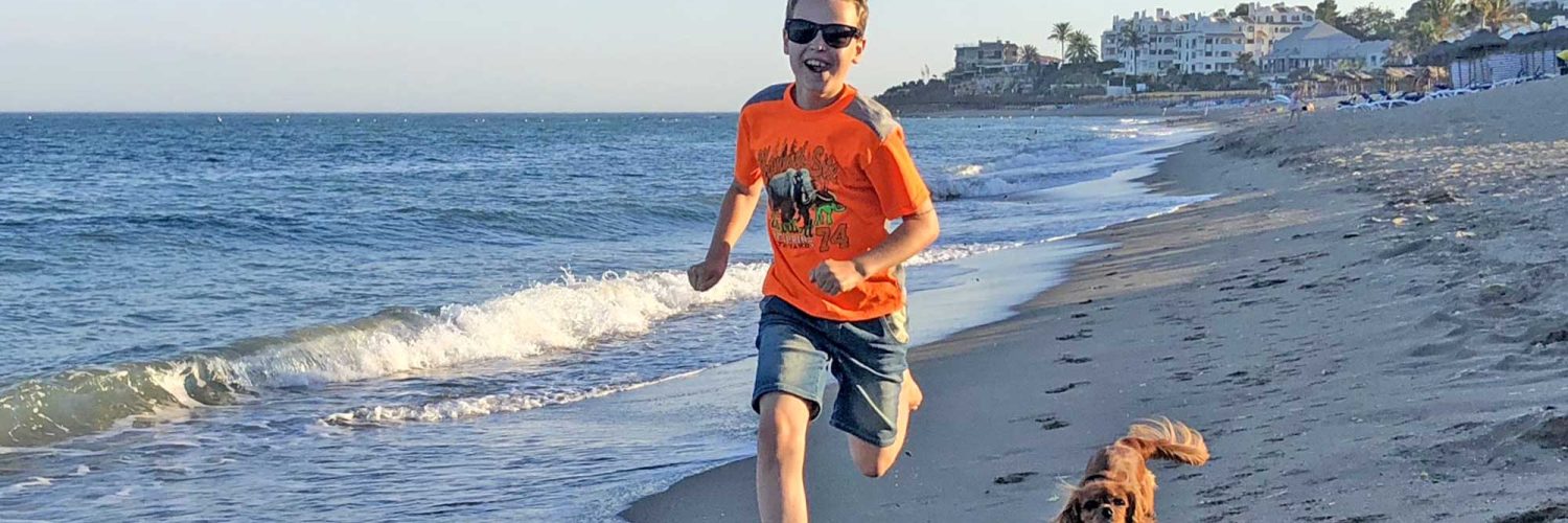 Gutt og hund som løper i på stranden.