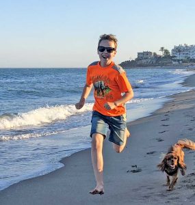 Gutt og hund som løper i på stranden.