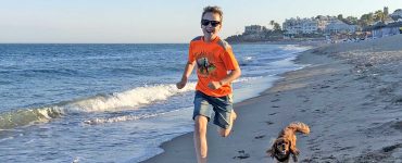 Gutt og hund som løper i på stranden.