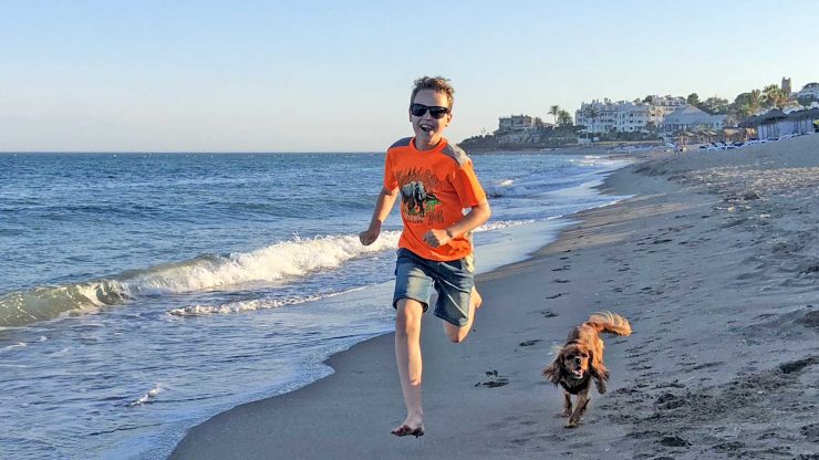 Gutt og hund som løper i på stranden.