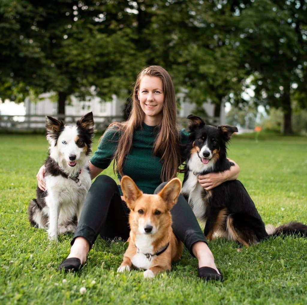 Frida Gulbrandsen - Dyr og folk Frida Gulbrandsen sitter på gresset sammen med tre hunder.